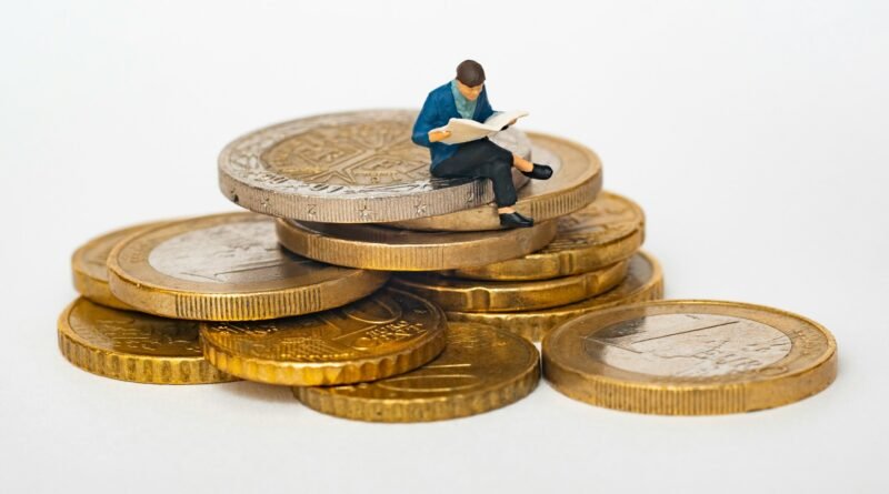 monedas apiladas y en el tope aparece una figurita de un hombre muy pequeño leyendo un libro.